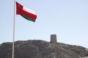 la bandera de Omán y al fondo una torre de la fortaleza